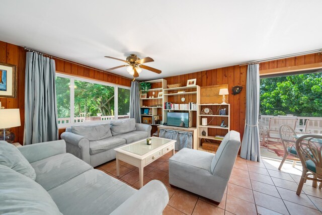 living room with ceiling fan, light tile patterned floors, and wood walls