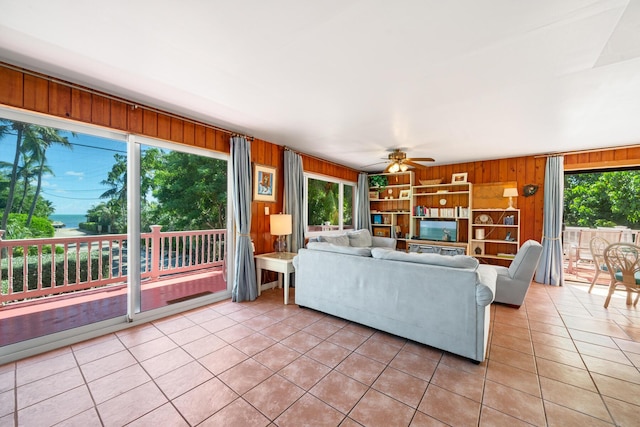 unfurnished living room featuring ceiling fan, plenty of natural light, wooden walls, and light tile patterned floors