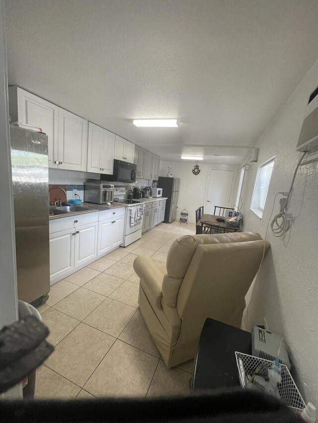 kitchen featuring light tile patterned flooring, sink, stainless steel fridge, electric stove, and white cabinets