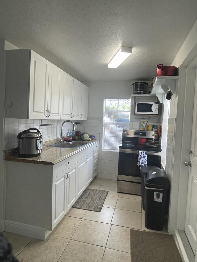 kitchen featuring white microwave, light tile patterned floors, electric range, white cabinetry, and a sink