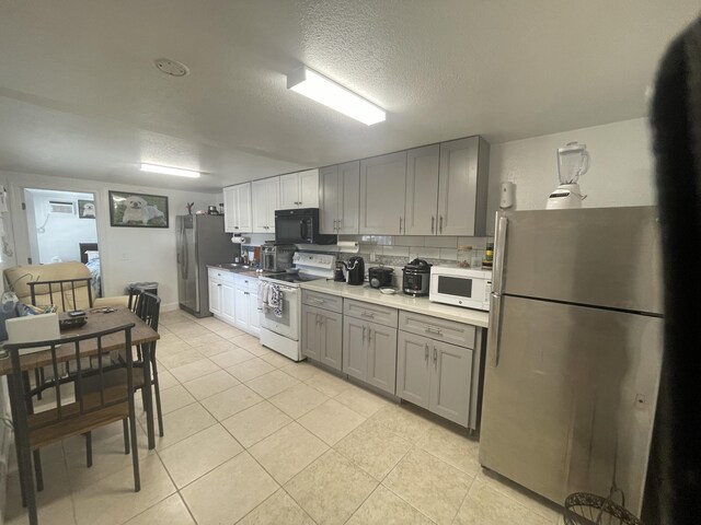 kitchen featuring gray cabinetry, a textured ceiling, light tile patterned floors, white appliances, and decorative backsplash