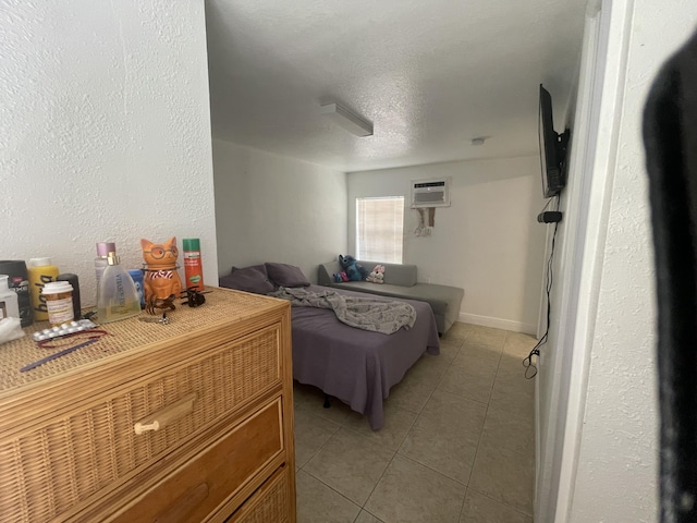 bedroom featuring light tile patterned floors, baseboards, a textured ceiling, and a wall unit AC