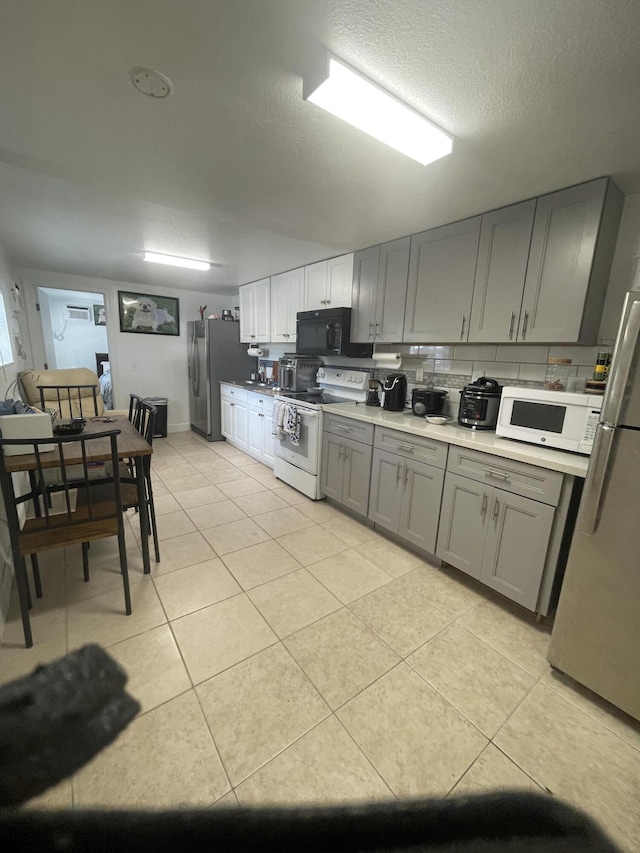 kitchen with white appliances, light tile patterned floors, gray cabinets, decorative backsplash, and a textured ceiling