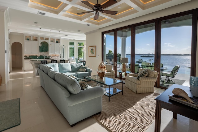 tiled living room with coffered ceiling, a water view, crown molding, ceiling fan, and a high ceiling