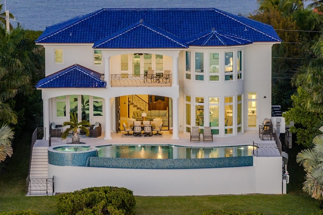 rear view of house with a swimming pool with hot tub, a patio area, and a balcony