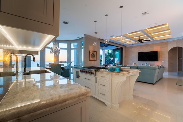 kitchen featuring stainless steel gas cooktop, white cabinetry, a center island, pendant lighting, and light stone countertops