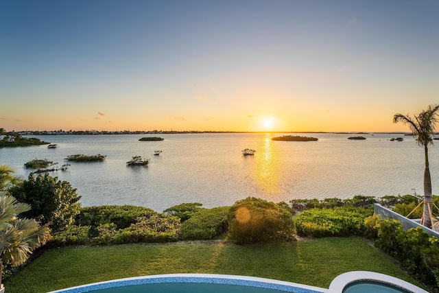 pool at dusk featuring a water view and a yard