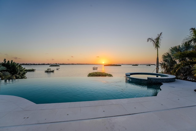 pool at dusk with a water view and an in ground hot tub