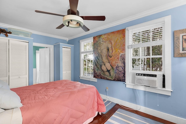 bedroom with ornamental molding, wood-type flooring, two closets, and ceiling fan