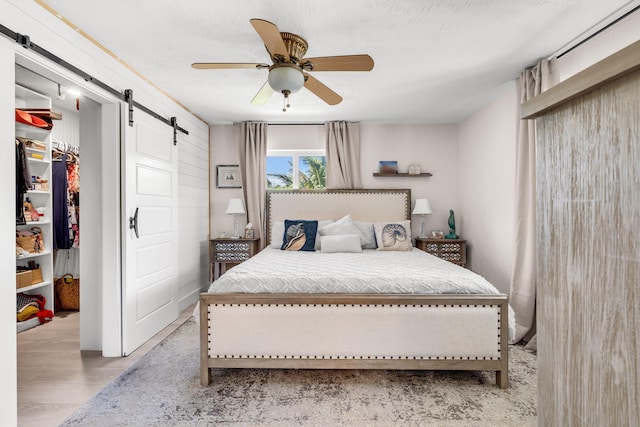 bedroom featuring ceiling fan, light hardwood / wood-style floors, a barn door, a spacious closet, and a closet