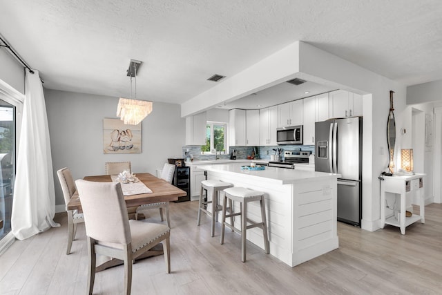 kitchen with a kitchen island, decorative light fixtures, white cabinetry, decorative backsplash, and stainless steel appliances