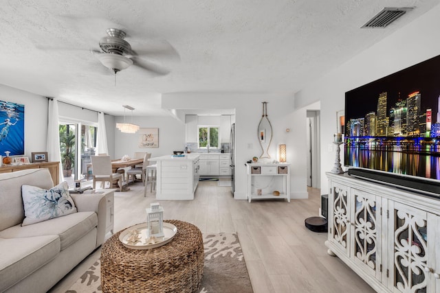 living room with ceiling fan, a healthy amount of sunlight, a textured ceiling, and light wood-type flooring