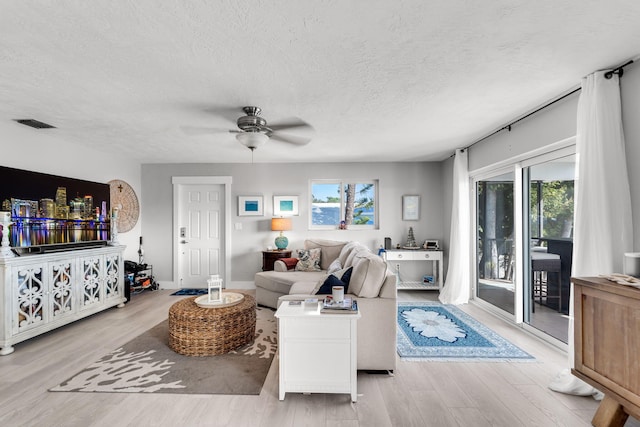 living room featuring ceiling fan, light hardwood / wood-style floors, and a textured ceiling