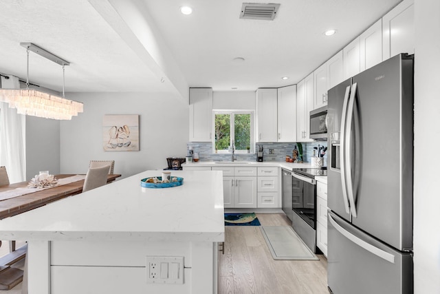 kitchen featuring sink, white cabinetry, hanging light fixtures, stainless steel appliances, and tasteful backsplash