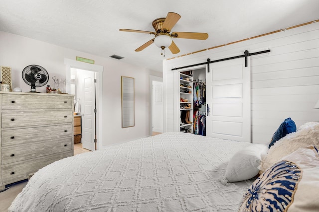 bedroom with a closet, ensuite bath, a barn door, and ceiling fan