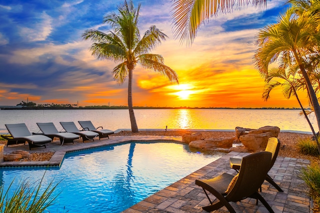 pool at dusk with a patio and a water view