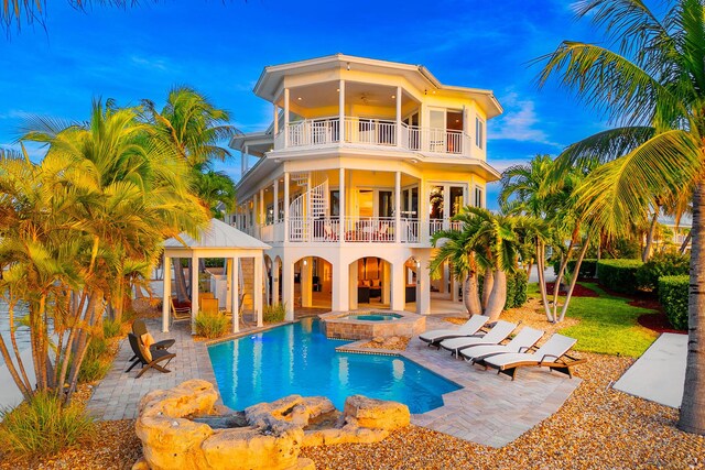 rear view of house featuring a swimming pool with hot tub, ceiling fan, a patio area, and a balcony