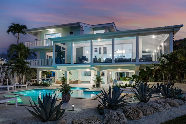 back house at dusk featuring a balcony and a patio