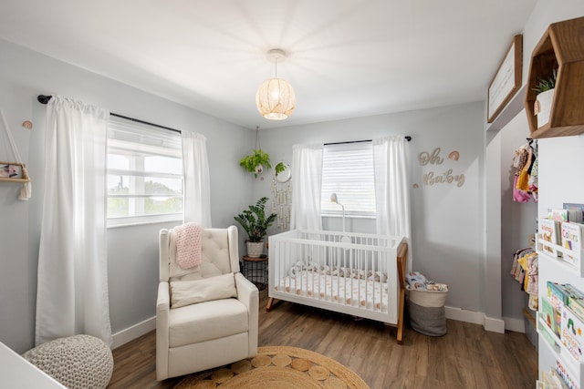 bedroom featuring multiple windows, dark wood-type flooring, and a crib