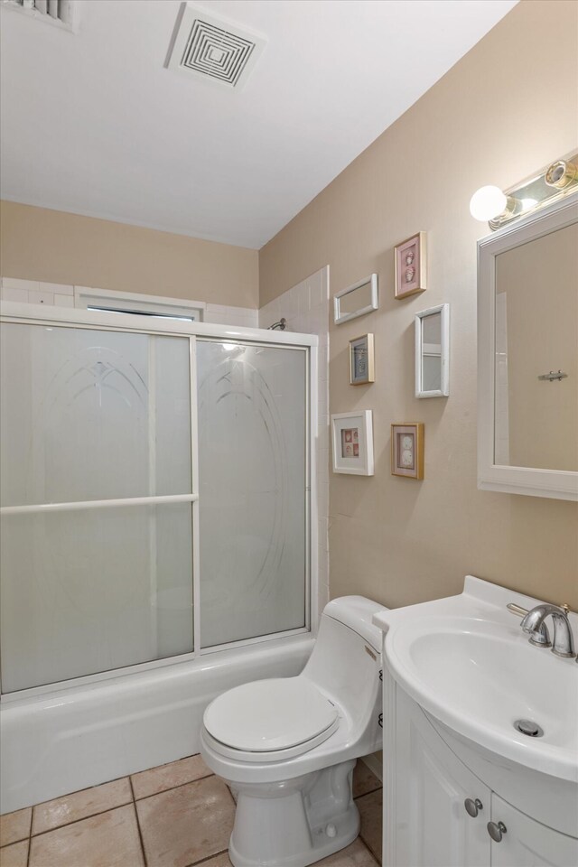 bathroom featuring visible vents, toilet, combined bath / shower with glass door, vanity, and tile patterned flooring