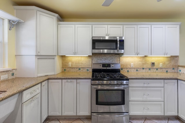 kitchen with light tile patterned floors, tasteful backsplash, white cabinets, appliances with stainless steel finishes, and light stone countertops