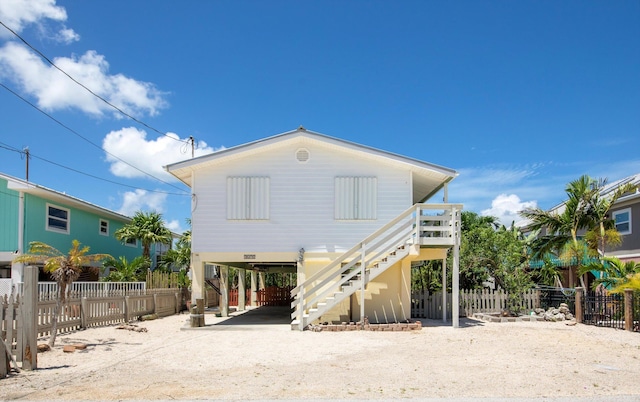 back of house featuring dirt driveway, a carport, stairway, and fence