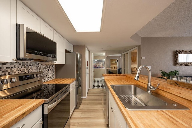 kitchen featuring a sink, stainless steel appliances, white cabinetry, and wood counters