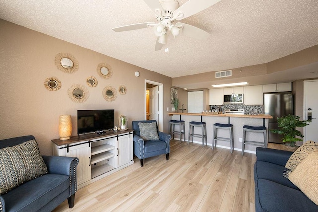 living room featuring ceiling fan, visible vents, a textured ceiling, and light wood-style flooring