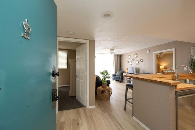 kitchen with ceiling fan, a sink, butcher block countertops, a textured ceiling, and light wood-type flooring