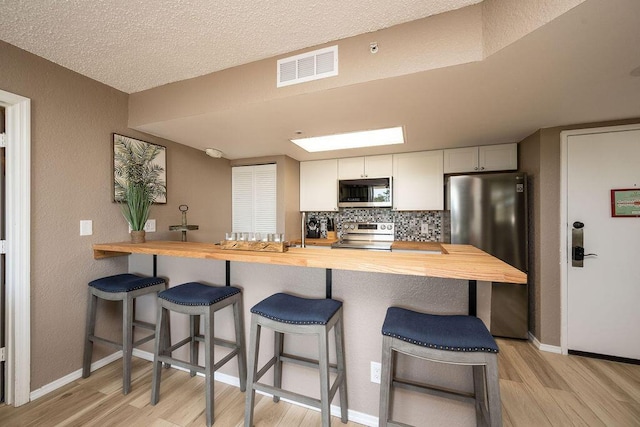 kitchen featuring visible vents, backsplash, butcher block counters, a breakfast bar area, and stainless steel appliances