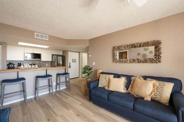 living area with light wood-type flooring, visible vents, and a textured ceiling