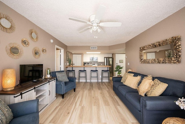 living room with visible vents, a textured ceiling, light wood-type flooring, and a ceiling fan