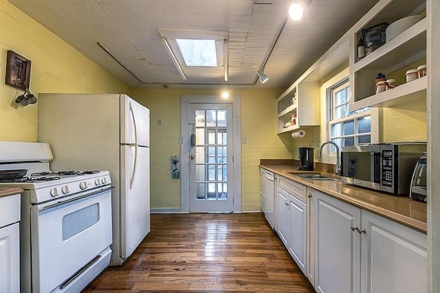 kitchen with a skylight, white cabinetry, sink, dark hardwood / wood-style flooring, and white appliances