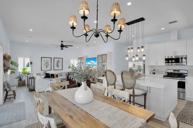 dining room with light hardwood / wood-style floors and ceiling fan with notable chandelier