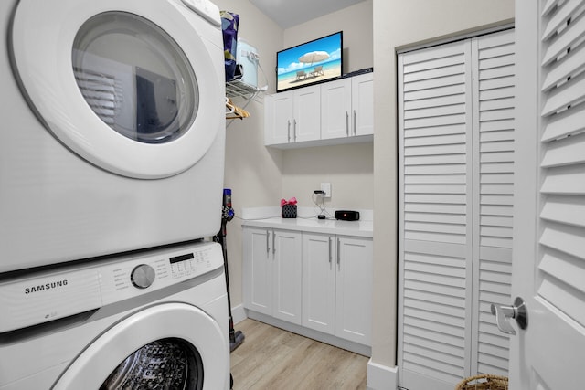 clothes washing area featuring cabinets, stacked washer and clothes dryer, and light wood-type flooring