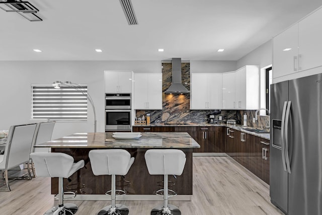 kitchen featuring a breakfast bar area, appliances with stainless steel finishes, a sink, wall chimney range hood, and modern cabinets