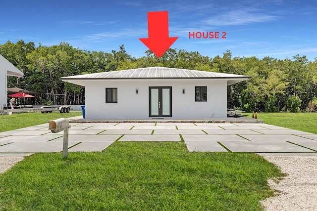 view of front facade with french doors, a patio, stucco siding, a front yard, and metal roof