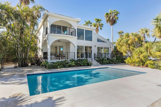 rear view of property featuring a fenced in pool, a patio area, and a balcony