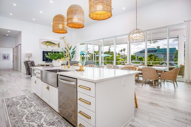 kitchen with hanging light fixtures, stainless steel dishwasher, a kitchen breakfast bar, a kitchen island with sink, and white cabinets