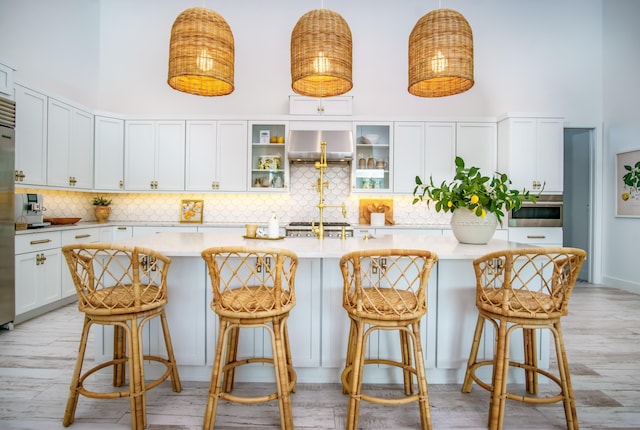 kitchen featuring a towering ceiling, a kitchen island with sink, a breakfast bar area, and decorative light fixtures