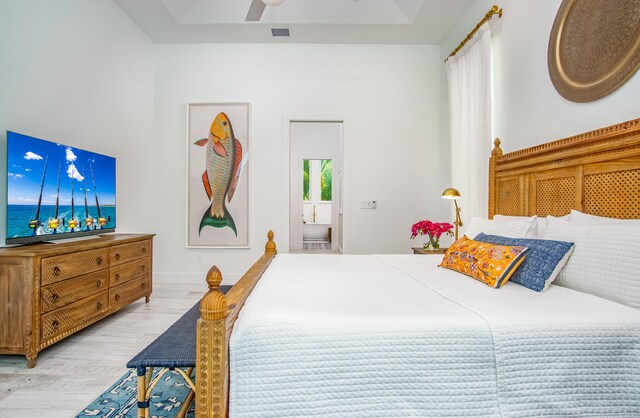 bedroom featuring light hardwood / wood-style flooring, a raised ceiling, and ceiling fan