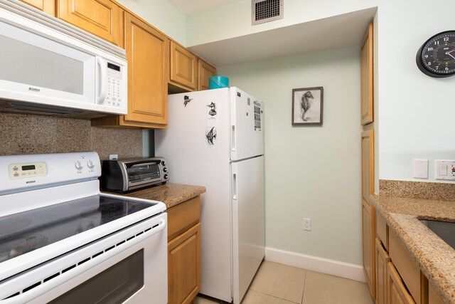 kitchen featuring white appliances, light stone countertops, and light tile patterned floors