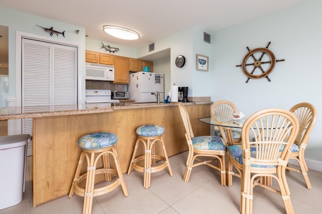 kitchen featuring white appliances, a breakfast bar area, kitchen peninsula, and decorative backsplash