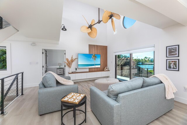 living area featuring a high ceiling, light wood-type flooring, a ceiling fan, and baseboards