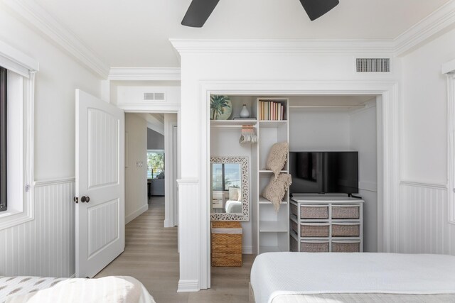 bedroom featuring crown molding, a closet, visible vents, light wood-style floors, and wainscoting