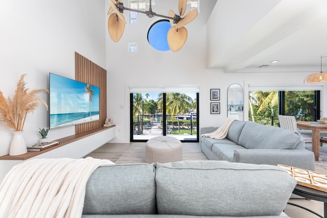 living area featuring a ceiling fan, light wood-style floors, plenty of natural light, and a high ceiling