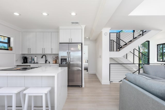 kitchen with stainless steel fridge, visible vents, light stone countertops, white cabinetry, and a wealth of natural light