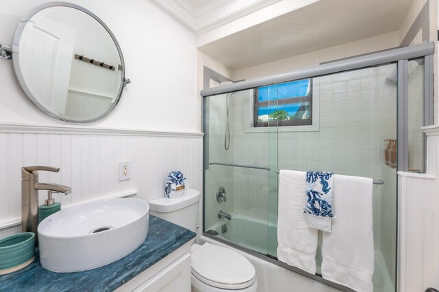 full bathroom with wainscoting, toilet, enclosed tub / shower combo, ornamental molding, and vanity