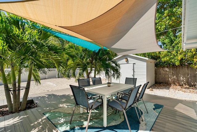 wooden deck with a storage unit, outdoor dining space, an outbuilding, and a fenced backyard