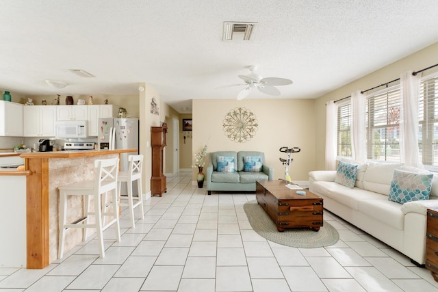 living room with ceiling fan, a textured ceiling, and light tile patterned flooring